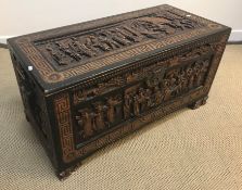 An Eastern ebonised and carved camphor wood trunk with all over figural panel decoration within