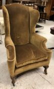 A late Victorian upholstered wing back scroll arm chair on cabriole front legs to pad feet,