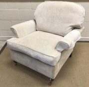 A modern upholstered scroll arm chair on turned front legs to brass caps and castors,