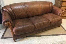 A modern brown leather upholstered three seat sofa with scroll arms and carved show frame over a