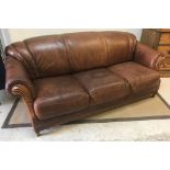 A modern brown leather upholstered three seat sofa with scroll arms and carved show frame over a