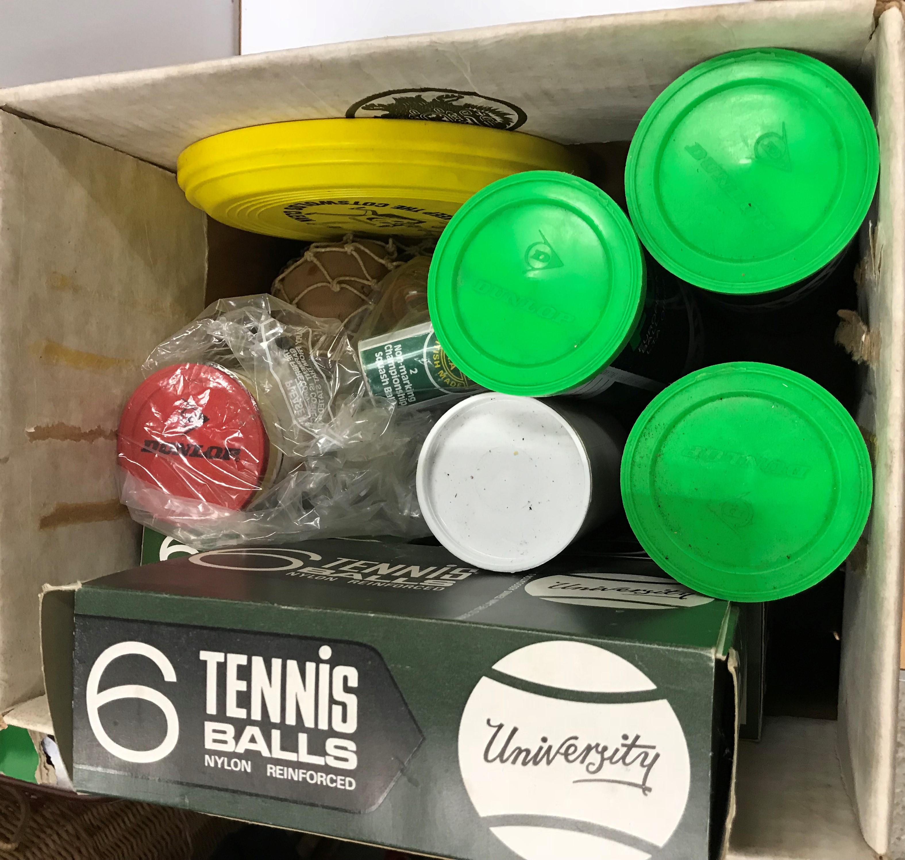 A box containing various tennis balls, squash balls, hockey balls, etc,
