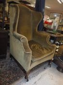 A late Victorian upholstered wing back scroll arm chair on cabriole front legs to pad feet,