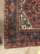 A Persian rug, the central panel set with lozenge shaped medallion on a red, blue and cream ground,