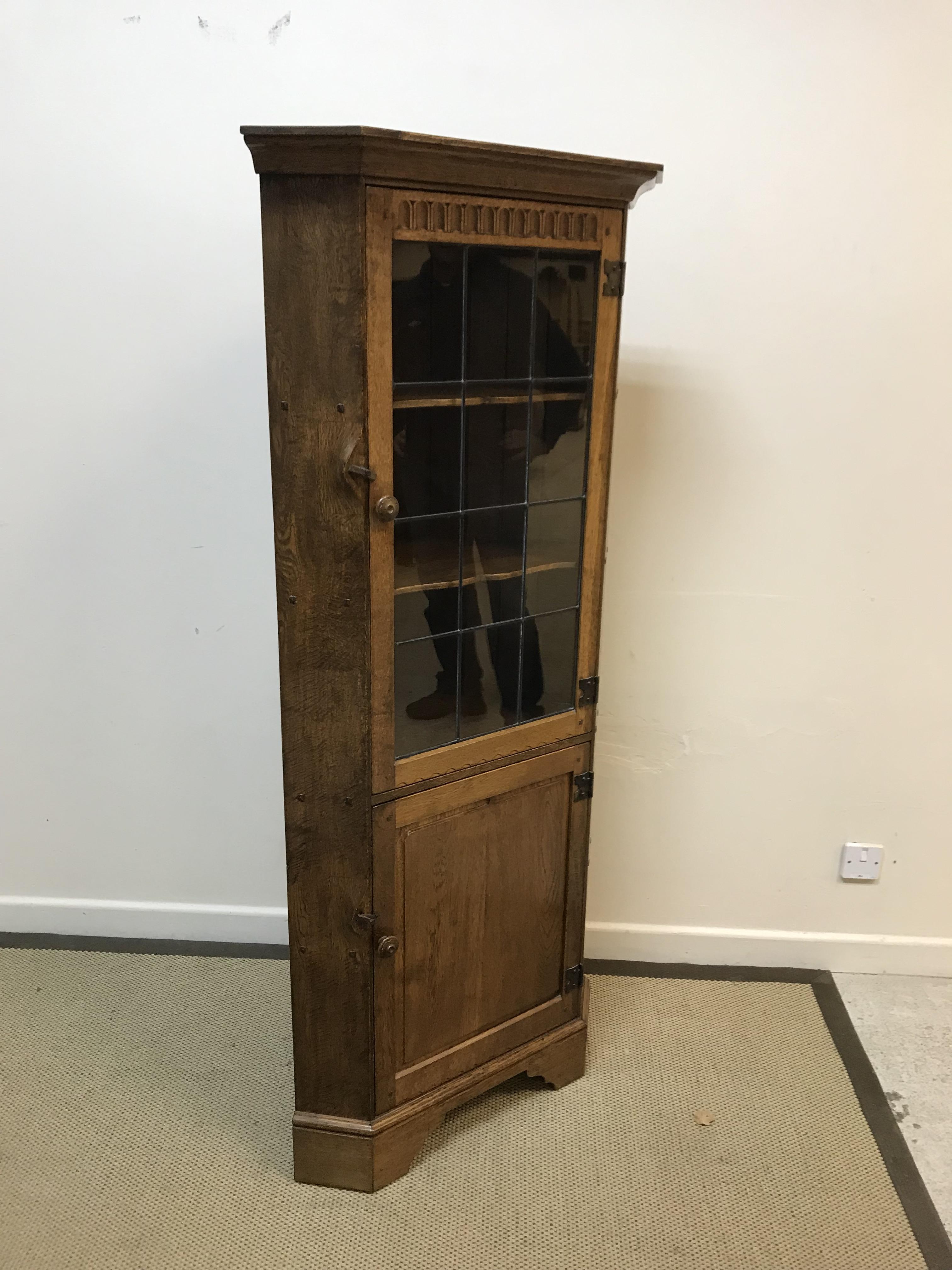 A modern oak free-standing corner cupboard with leaded glazed door enclosing two shelves over a