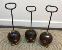 A collection of three wooden lawn bowls doorstops with iron handles on brass feet,