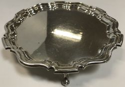 A silver salver in the Georgian manner with pie-crust rim raised on three scroll feet (by William