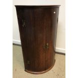 An early 19th Century oak bow fronted hanging corner cupboard,