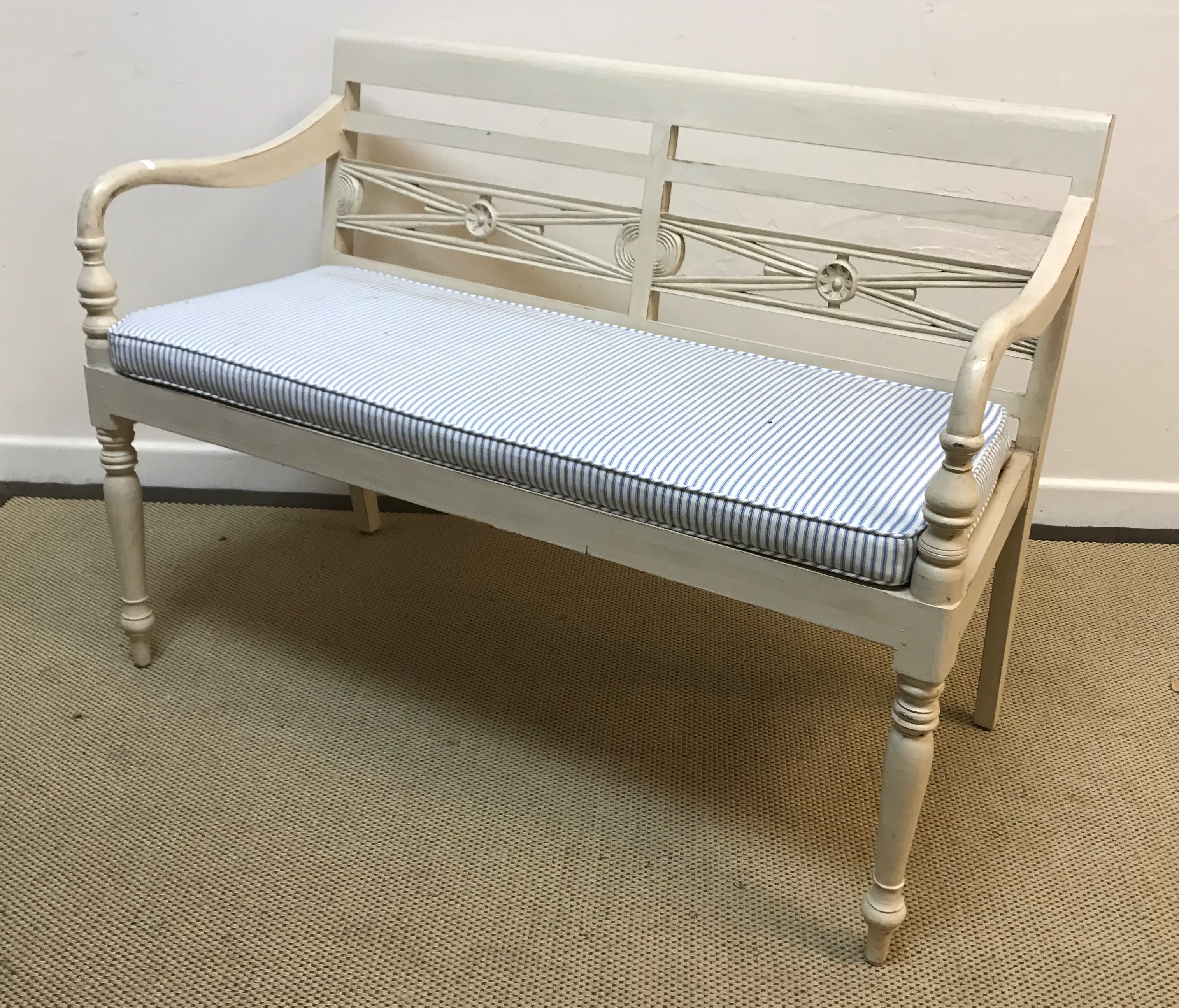 A white painted bench seat in the manner of OKA with medallion decorated slat back over open arms