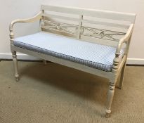 A white painted bench seat in the manner of OKA with medallion decorated slat back over open arms