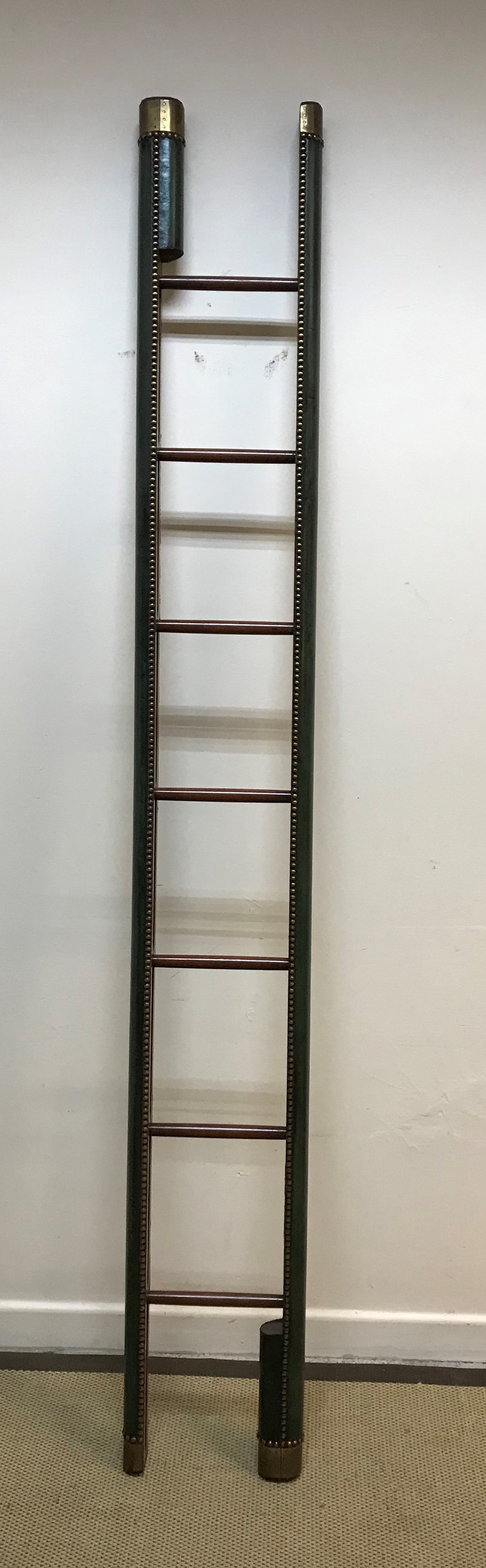 A brass studded green leather covered library ladder in the 19th Century manner with mahogany rungs,