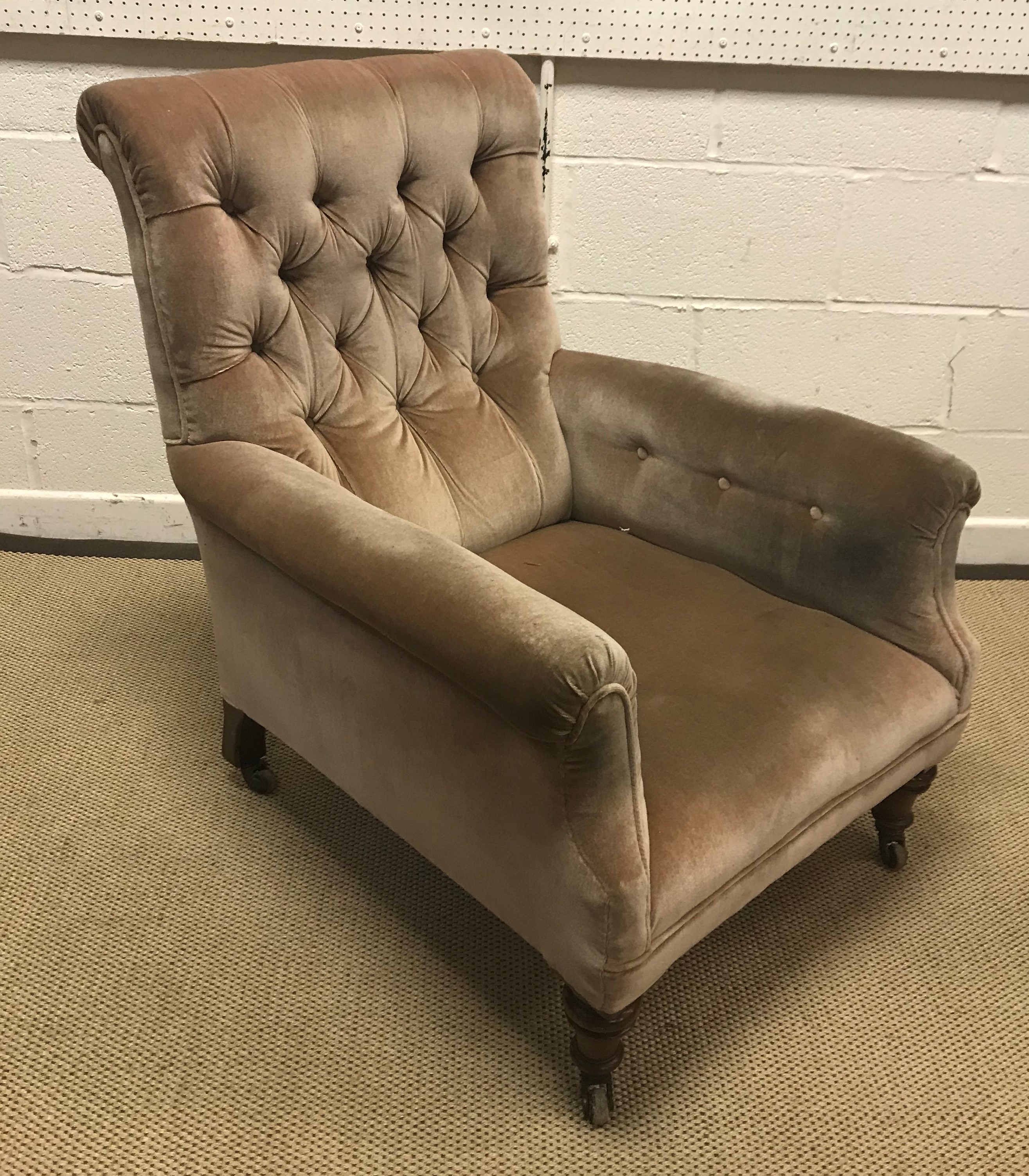 A late Victorian button upholstered scroll arm chair on turned and ringed front legs to brass caps