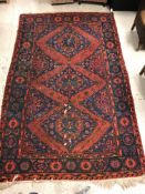 A Persian rug with three repeating lozenge medallions on a red and blue ground, within a blue, red