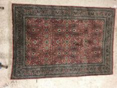 A Persian rug, the central panel set with all-over floral decoration on a pink ground, within a