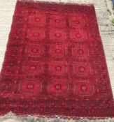 A Bokhara rug with repeating medallions on a red ground, within a red and black stepped geometric