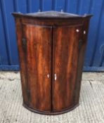 A 19th Century mahogany bow fronted corner cupboard, the two figured doors with ivory kite shaped
