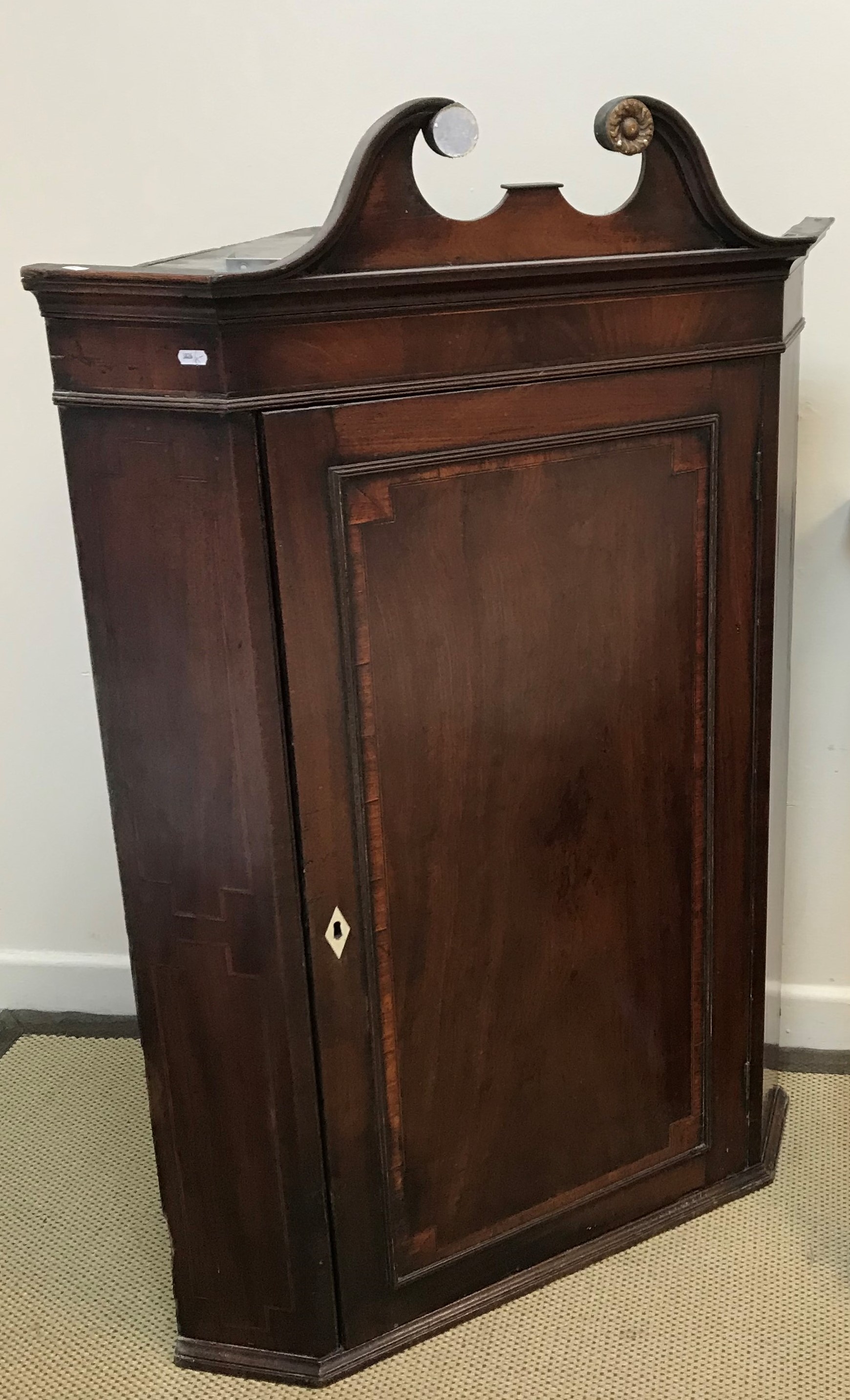 An early 19th Century mahogany and inlaid hanging corner cupboard with broken arch pediment over a