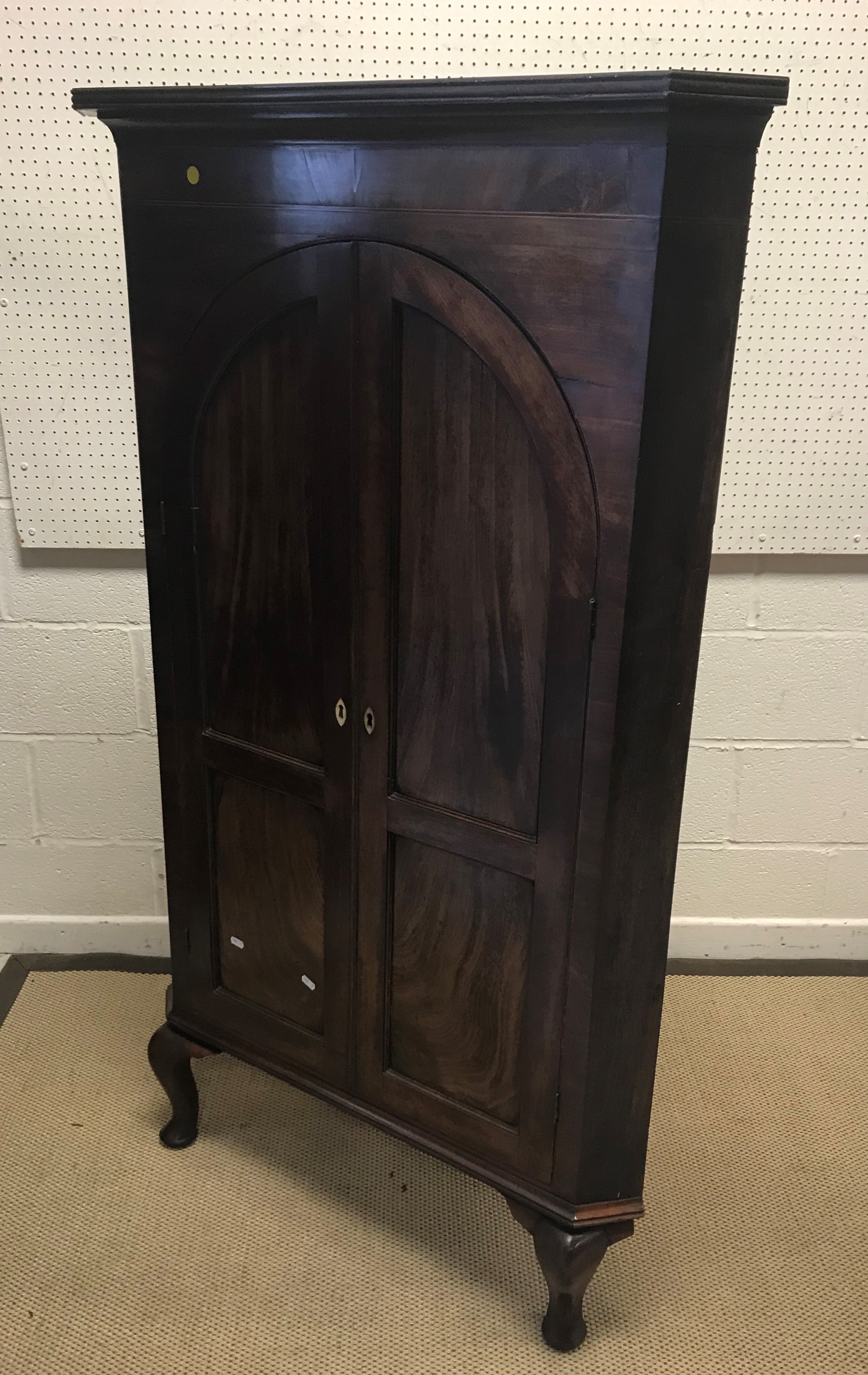 A late George III mahogany corner cupboard, the moulded cornice over two arch panelled doors