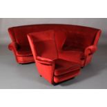 A curved sofa with winged arms in red buttoned velvet, on castors, together with a winged armchair