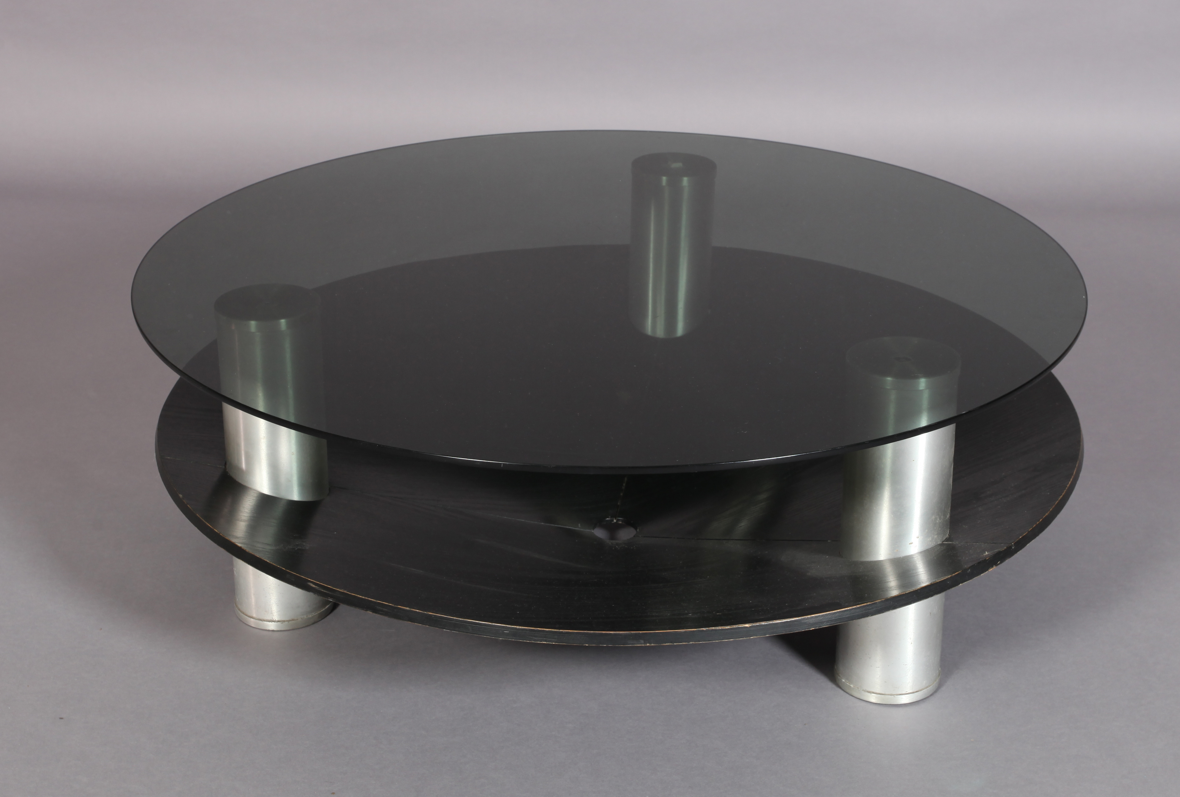 A circular two tier coffee table, the smoked glass top supported on three cylindrical aluminum