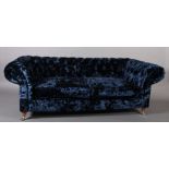 A three seater sofa upholstered in royal blue crushed velvet, on turned legs with chrome castors,