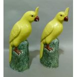 A pair of Chinese porcelain models of yellow parakeets with red beaks and feet standing on green