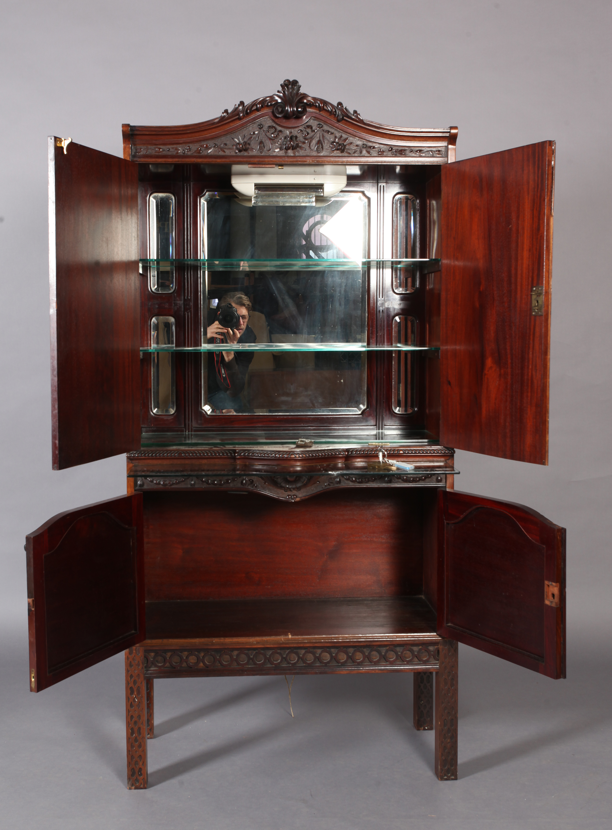 An Edwardian mahogany drinks cabinet with ornate foliate carved serpentine top, the frieze carved