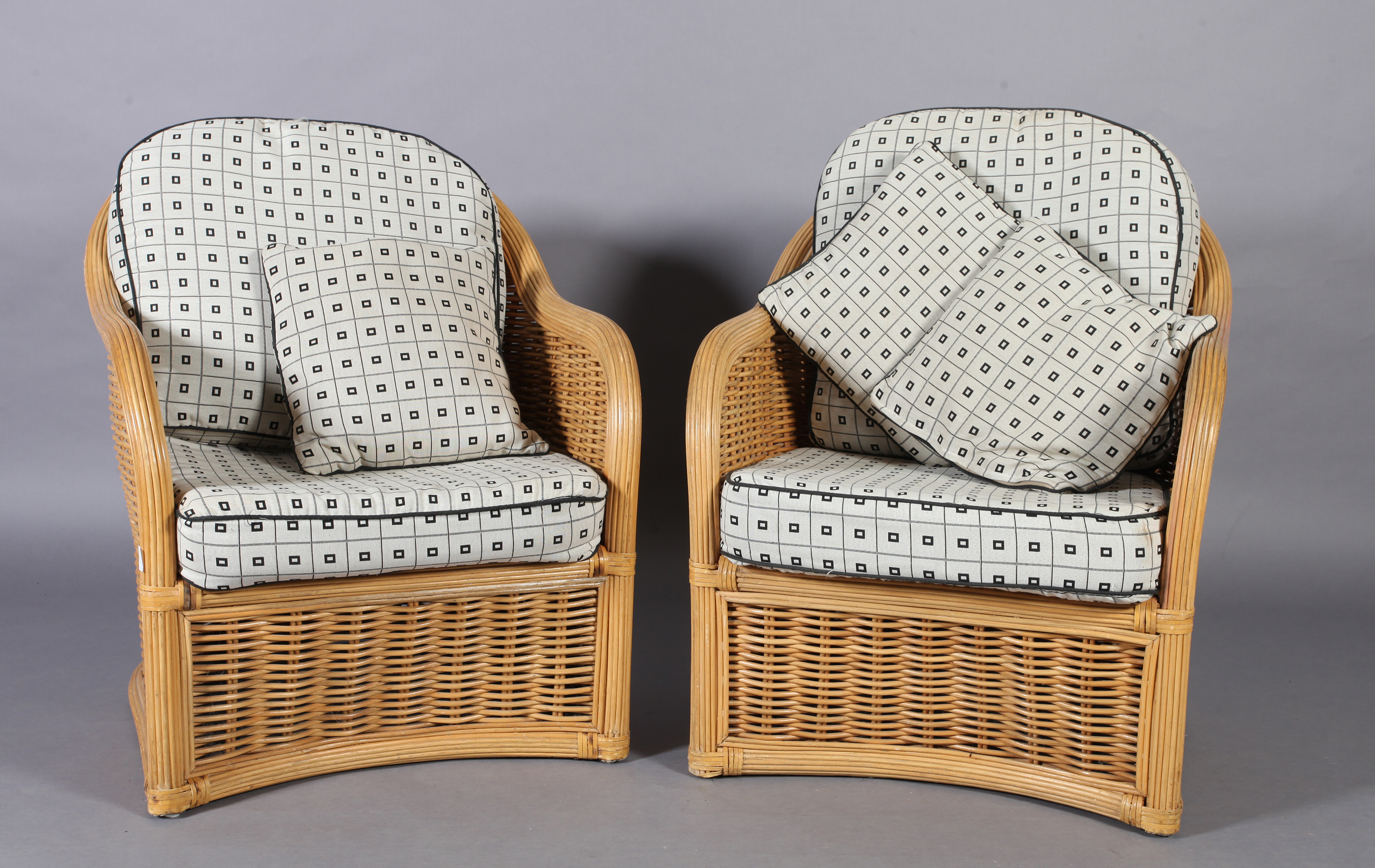 A pair of wicker elbow chairs with loose cushions