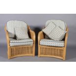 A pair of wicker elbow chairs with loose cushions