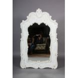 A modern white painted wooden wall mirror, rudimentary carved with foliate and C-scrolls around a