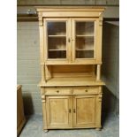 A Continental pine cabinet with flared cornice above a pair of glazed doors, panelled back and