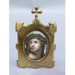 A head and shoulders portrait of Christ, printed on ceramic plaque held within a brass frame with