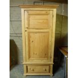 A pine wardrobe with flared cornice enclosed by a twin panelled door above panelled drawer