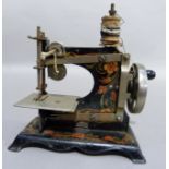 A child's early 20th century German black japanned tin sewing machine decorated in red and gold,
