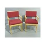 A pair of beech framed carvers upholstered in crimson to the back and seats each with a bookrest