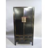 A reproduction Chinese style black lacquer wardrobe enclosed by a pair of doors, four short