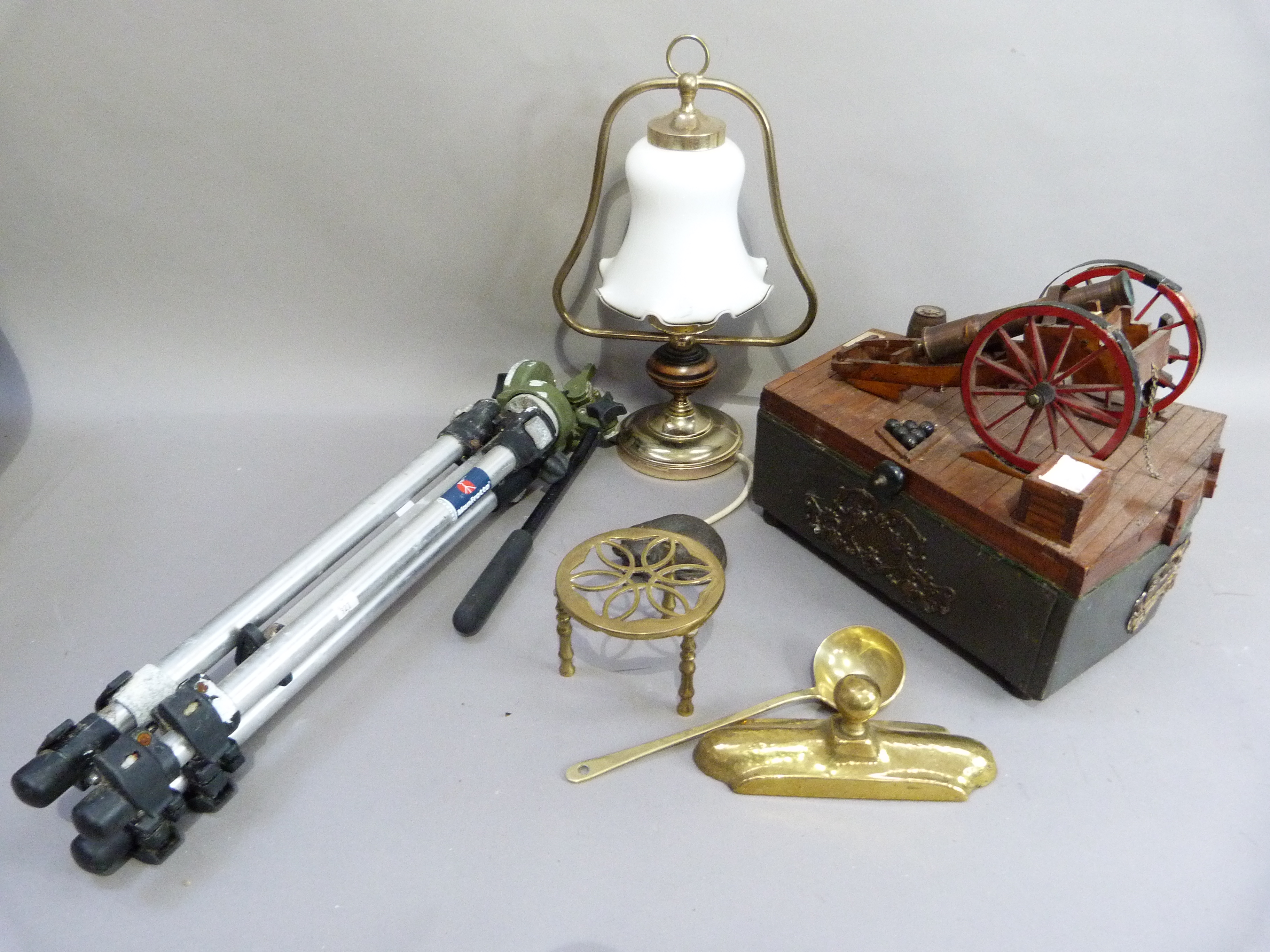 A canon mounted box, brass trivet, ladle, model of a cat, tripod and a lamp