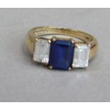 A three stone ring in 9ct gold, claw set to the centre with a step cut synthetic sapphire flanked by
