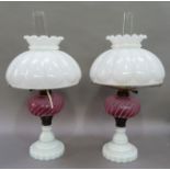 A pair of Victorian milk glass oil lamps with cranberry writhern glass reservoirs on a circular