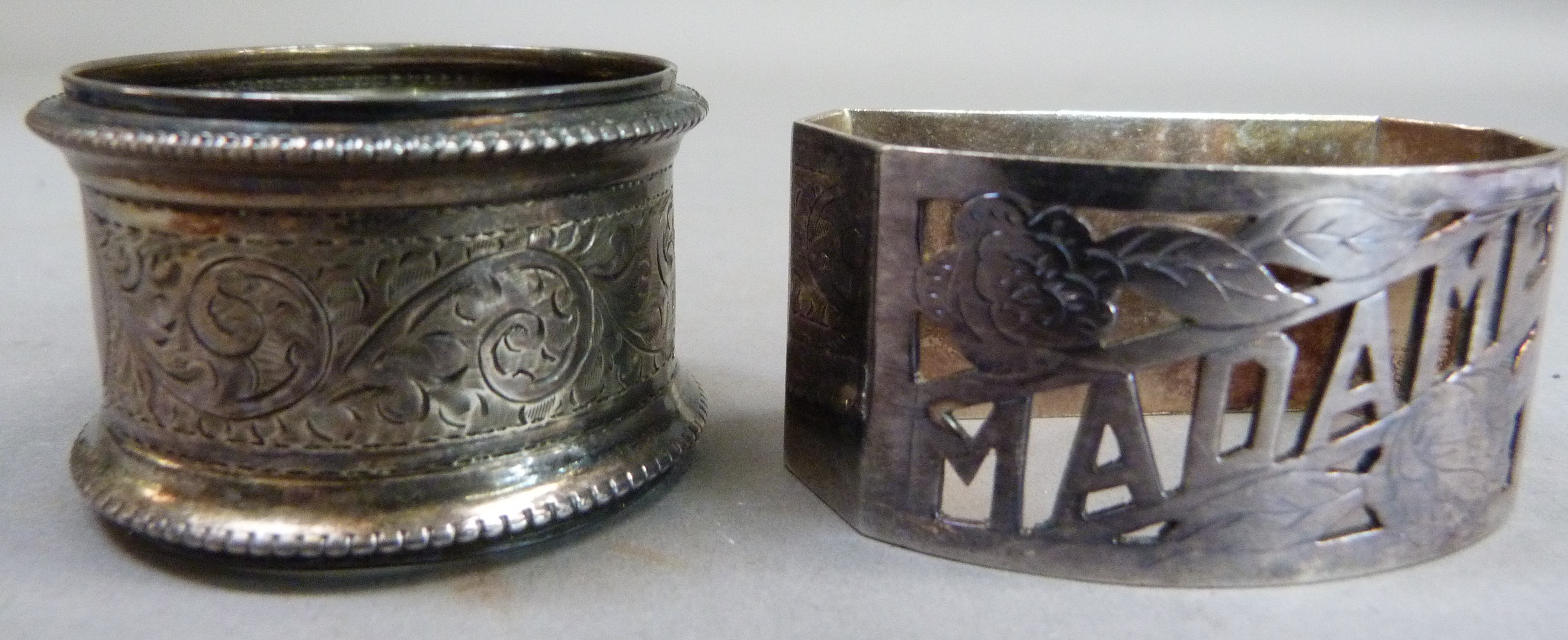 A silver napkin ring engraved with foliate leaf curls, with initial together with a white metal
