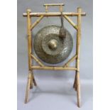 An early 20th century planished brass dinner gong with central boss hung from a bamboo frame,