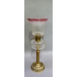 An Edwardian brass oil lamp having a cranberry tinted and opaque shade, clear glass reservoir and