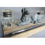 A desk stand mounted with a spelter figure of a recumbent dog, flanked by a glass inkwell to