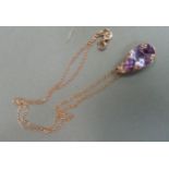 An amethyst pendant in rose gilt silver, the oval facetted stone claw set raised against a scroll