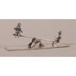 MINIATURES - A DUTCH SILVER SEESAW, one figure sitting sideways on, scrolling support, rectangular