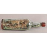 A VINTAGE SHIP IN A BOTTLE, the three masted sailing vessel with small ship and cottages beyond,