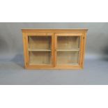 A reproduction pine hanging display cabinet with flared cornice enclosed by a pair of glazed