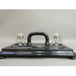 A Victorian ebonised ink stand of rounded rectangular form set with pair of wells, arched handle and