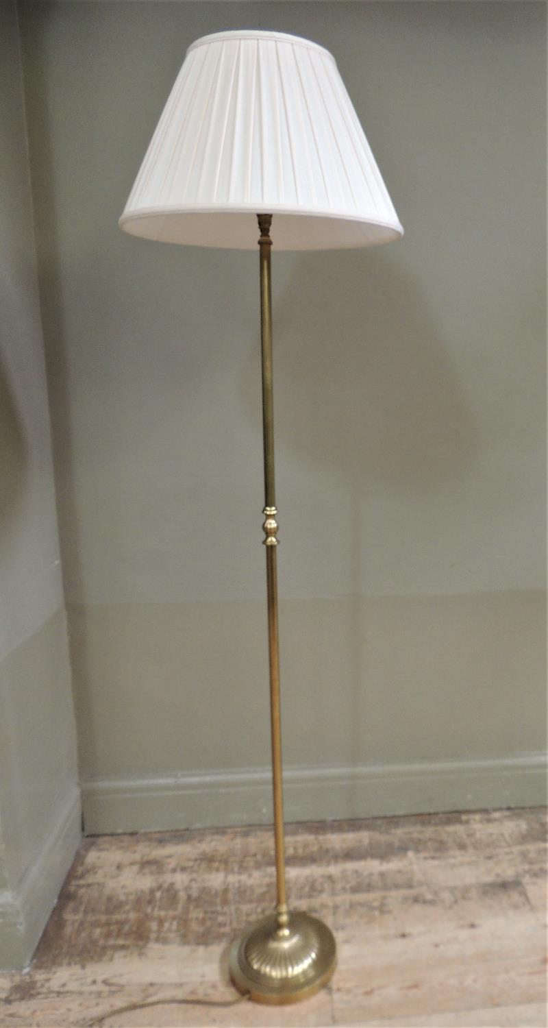A brass standard lamp of column form on fluted circular base with pleated pale apricot cotton shade,
