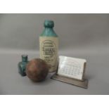 A silver plated desk calendar, a blue glass bottle, a cricket ball and a stone ginger beer bottle by
